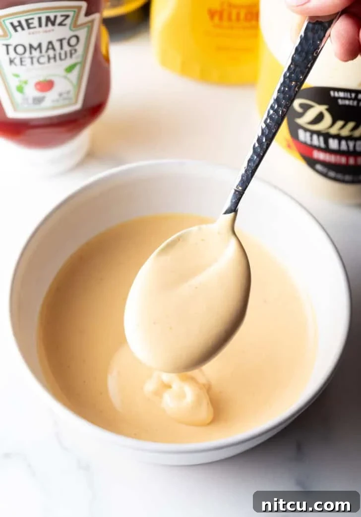 A spoon full of homemade burger sauce is held over a bowl of the creamy condiment, ready to be served.