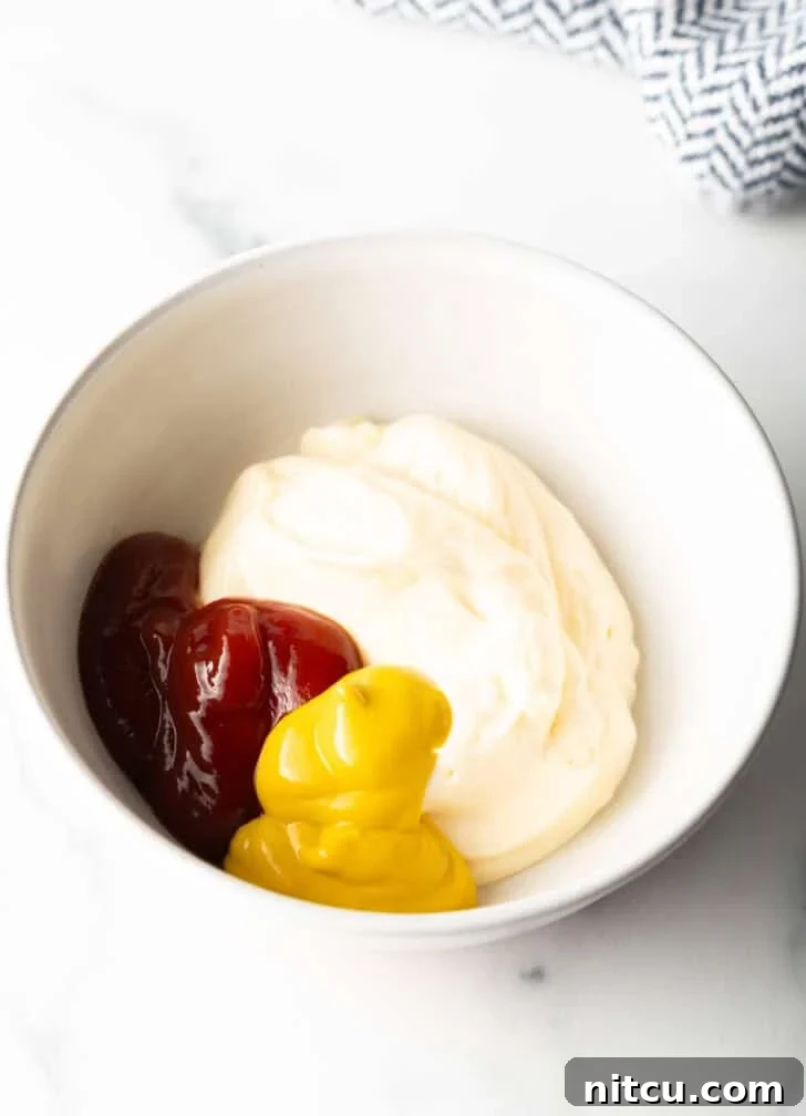 Mayonnaise, yellow mustard, and ketchup are combined in a pristine white mixing bowl, ready to be whisked into a sauce.