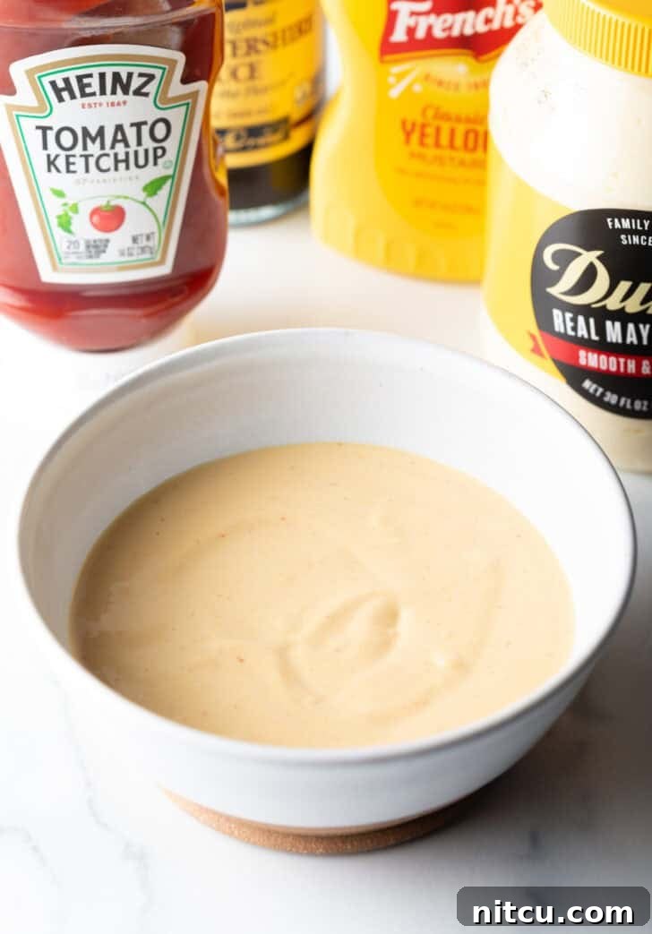 A creamy, orange-hued homemade burger sauce is presented in a white bowl, perfectly blended and ready for use.