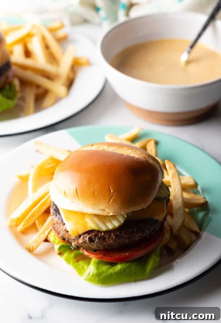 A close-up of a perfectly constructed cheeseburger, featuring fresh lettuce, juicy tomato, melted cheese, and a generous application of homemade burger sauce, presented on a white plate.