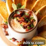 White cup with whipped feta with chopped sun dried tomato, on a plate surrounded by slices of toasted baguette.