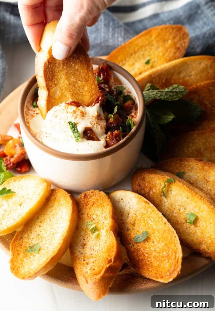 Hand dipping a slice of toasted baguette into a bowl of creamy whipped feta dip.