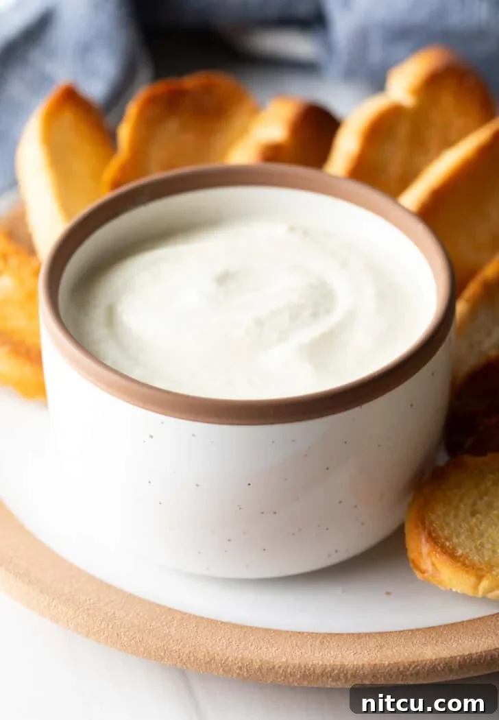 Creamy feta dip in a white bowl, on a plate with slices of toasted bread.