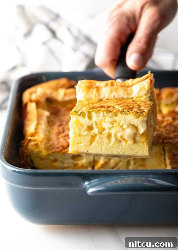 Hand carefully removing a perfectly baked square of golden egg casserole with a spatula from a square baking dish.