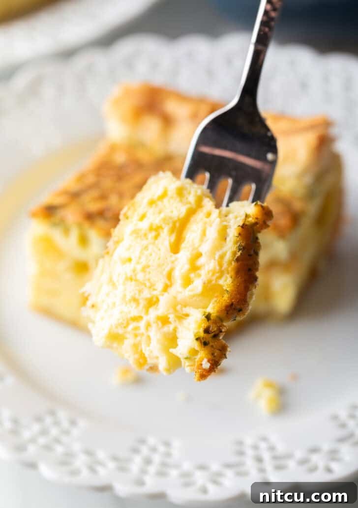 A fork proudly holds up a perfect mouthful of fluffy, golden egg casserole, showcasing its tender texture.