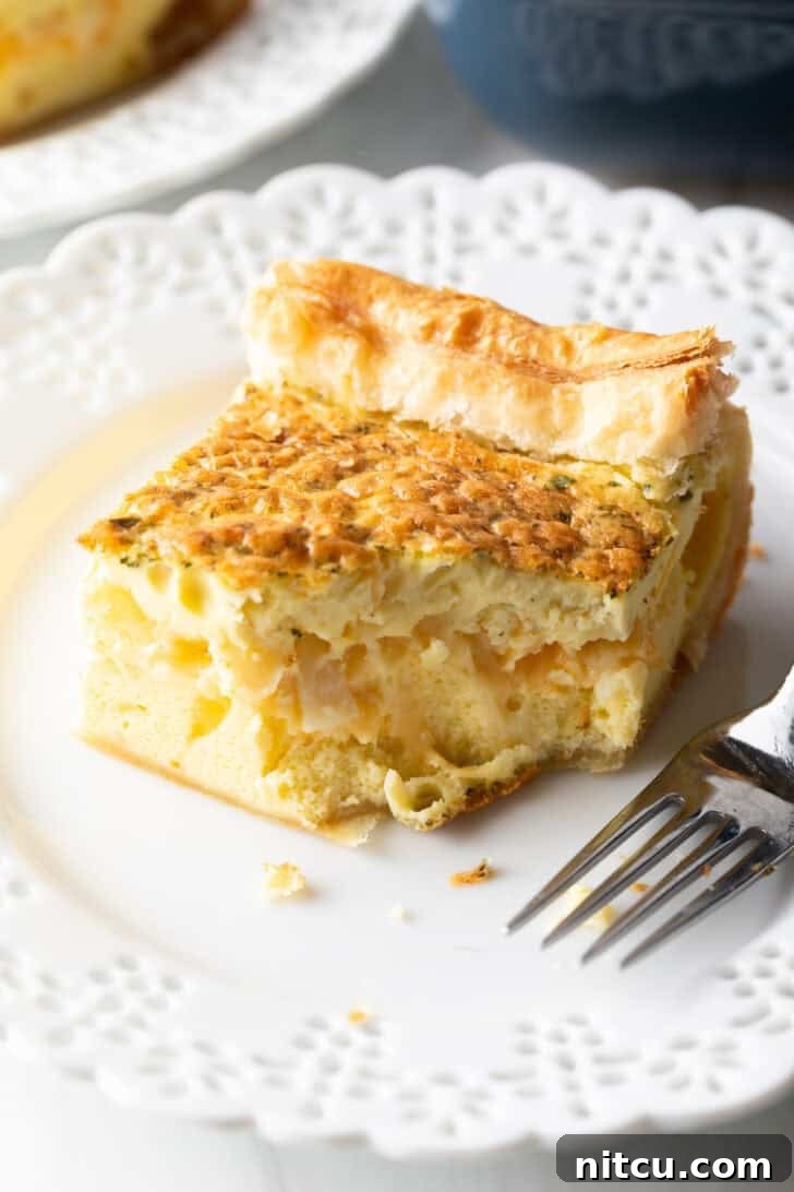 A perfectly portioned square of fluffy egg casserole resting on a pristine white plate, accompanied by a fork.