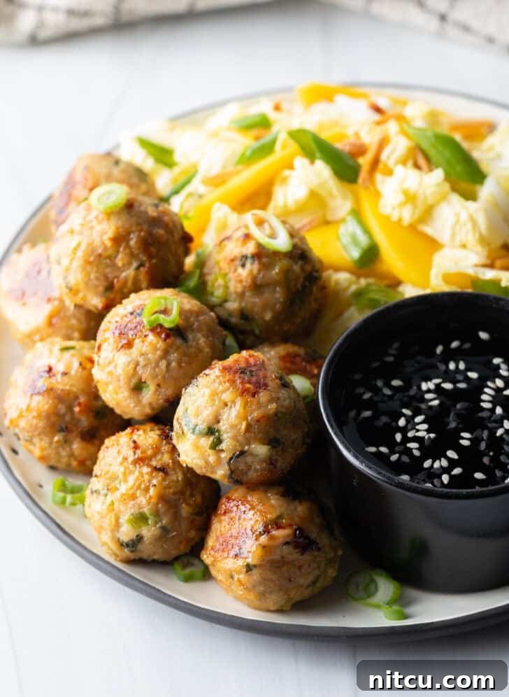 Plate of Thai turkey meatballs served with a vibrant Asian chopped salad and a small black bowl of dipping sauce.