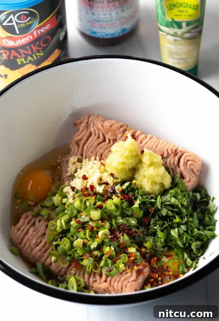 Ground turkey, minced lemongrass, whisked egg, and fresh basil in a white mixing bowl, ready to be combined.