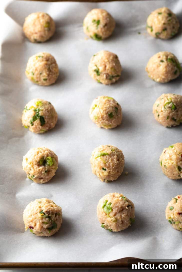 Fifteen raw, perfectly shaped turkey meatballs arranged on a parchment-lined baking sheet, ready for the oven.