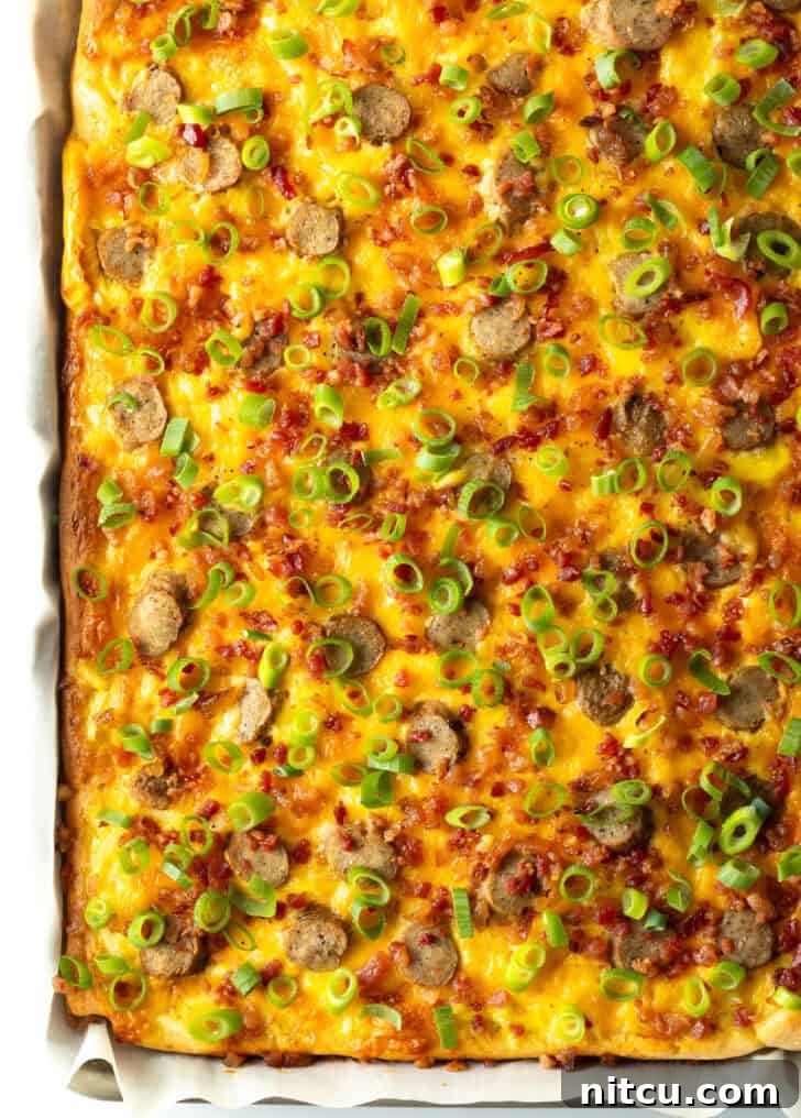 A beautifully presented rectangle baking sheet tray holding the finished breakfast pizza, lavishly topped with melted cheese, savory sausage, and vibrant green onions. The pizza is ready to be sliced and served.