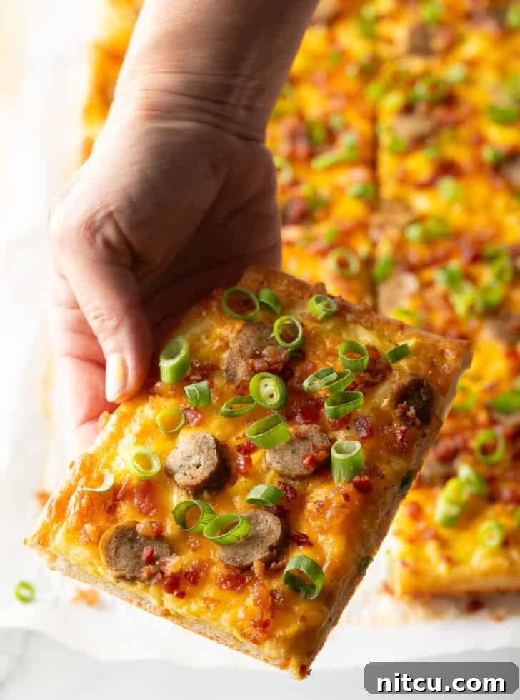 A rectangular baking sheet tray showcasing a freshly baked breakfast pizza, lavishly topped with melted cheese, savory sausage, and fresh green onions. The pizza has been expertly cut into 8 rectangular portions, with a hand reaching in to pull one inviting slice away, ready to be enjoyed.