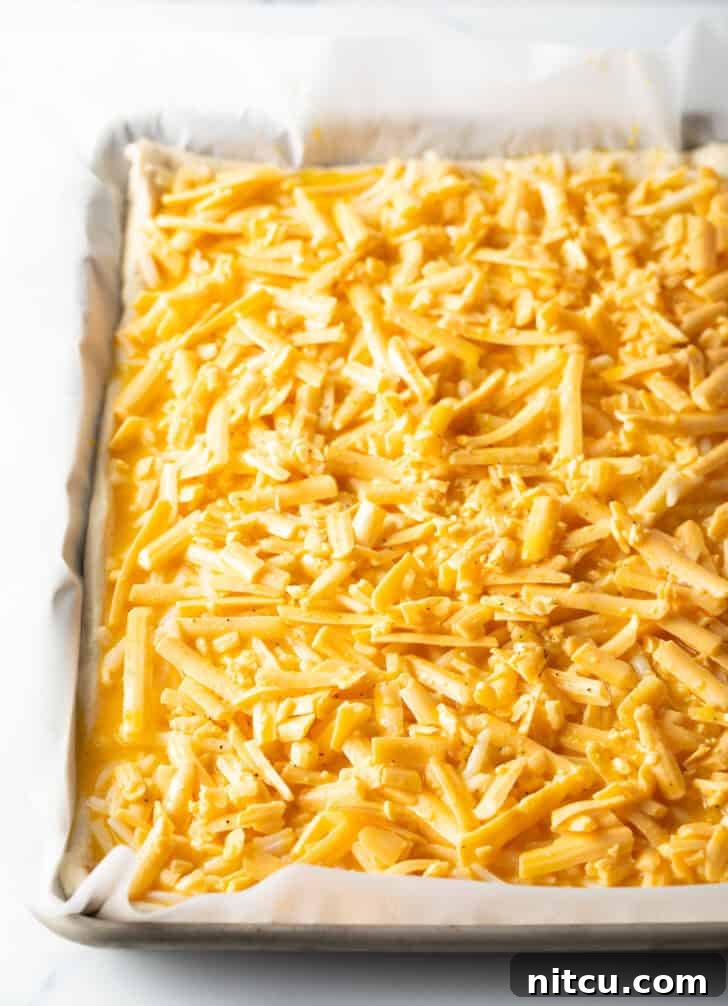 Another angle of an unbaked rectangular pizza, this time featuring a bountiful topping of shredded cheddar cheese, promising a rich, savory flavor.