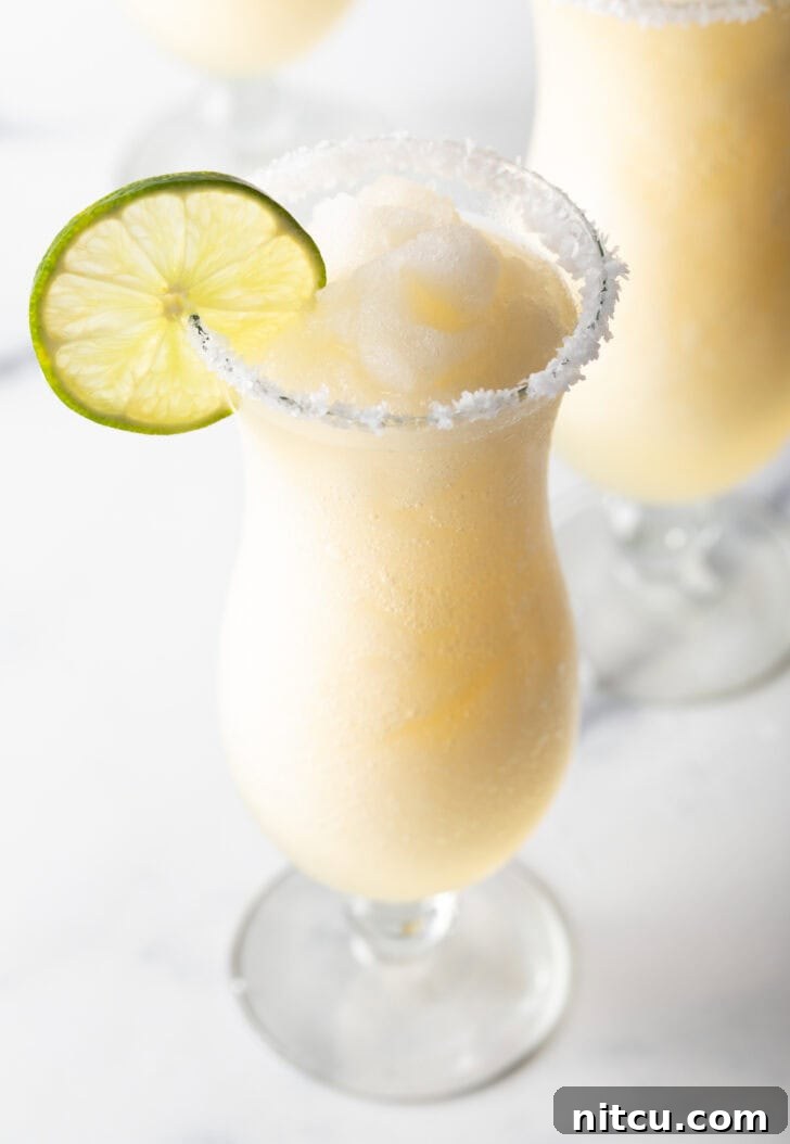 Frozen margarita in a hurricane glass, garnished with a slice of lime and salt around the rim.