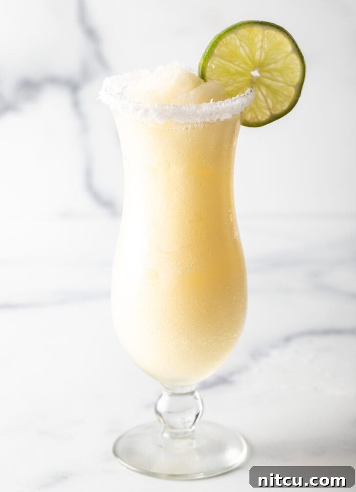 Frozen margarita in a hurricane glass, garnished with a slice of lime and salt around the rim.