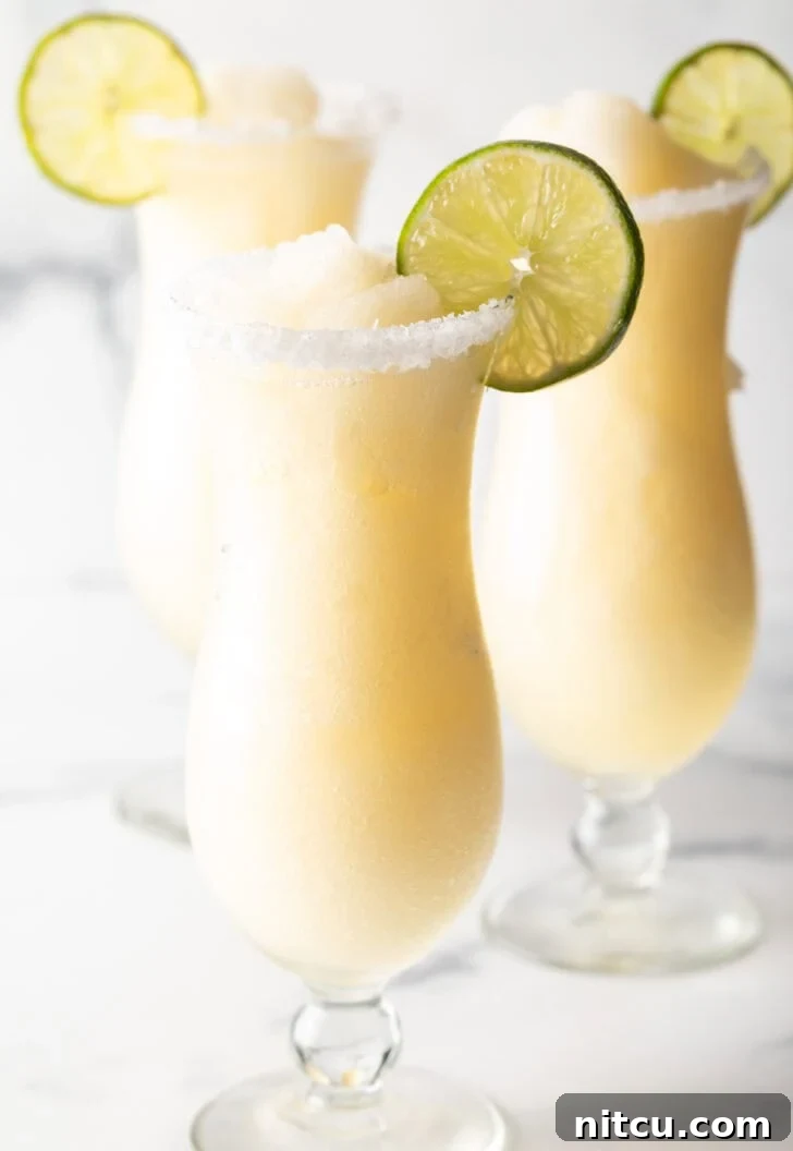 3 frozen margaritas in hurricane glasses, each garnished with a slice of lime and salt around the rim.