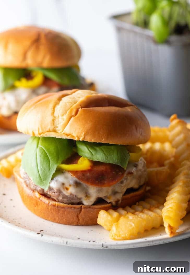 A delectable pizza burger resting on a white and black speckled plate, accompanied by a generous serving of perfectly golden crinkle-cut french fries.