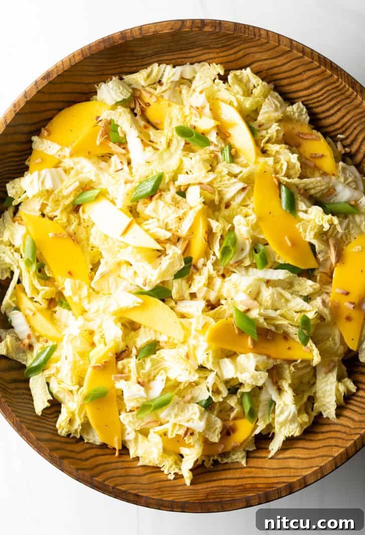 Top down view wood bowl with green napa cabbage, mango slices, and green onions.