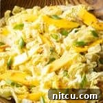 Wood bowl with green napa cabbage, mango slices, and green onions.