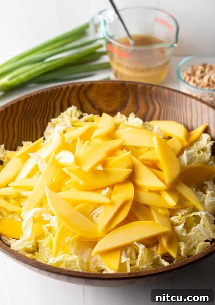 Slices of mango on top of shredded napa cabbage in a wood bowl.