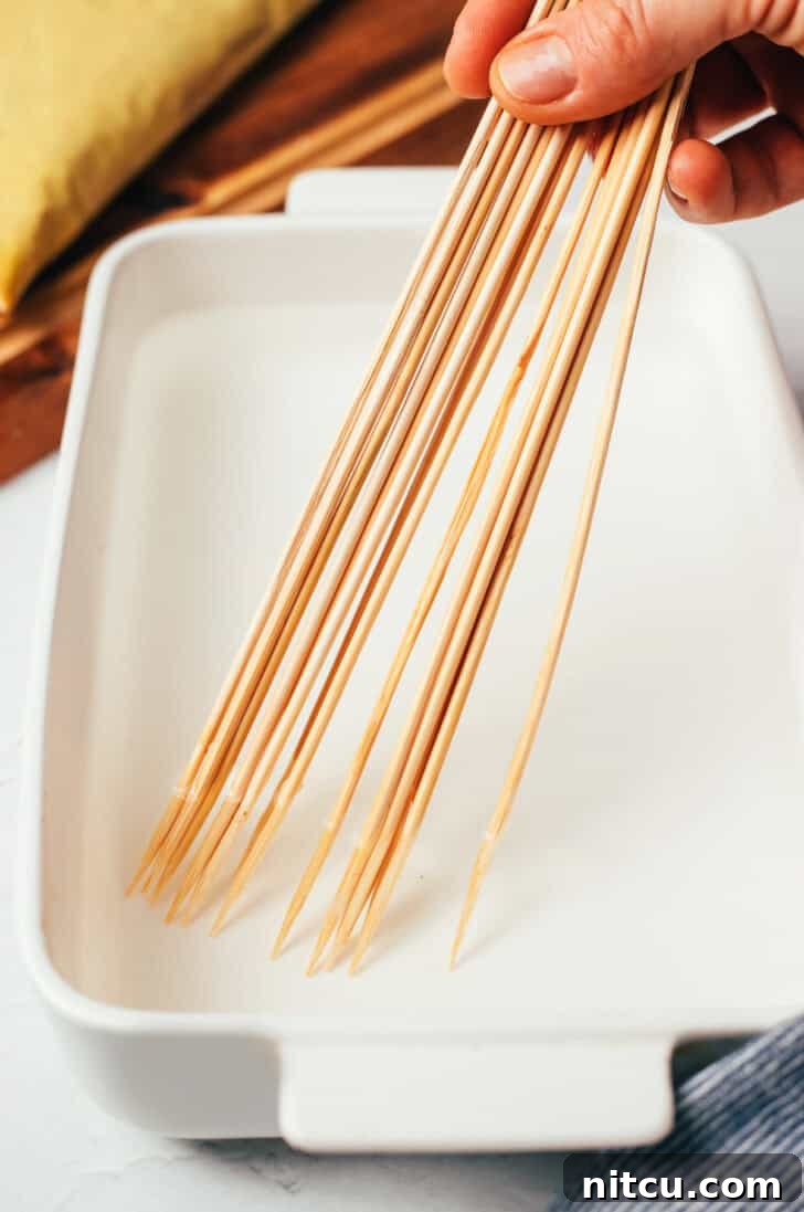 A handful of wooden skewers submerged in water within a white rectangular baking dish, demonstrating the essential soaking step.