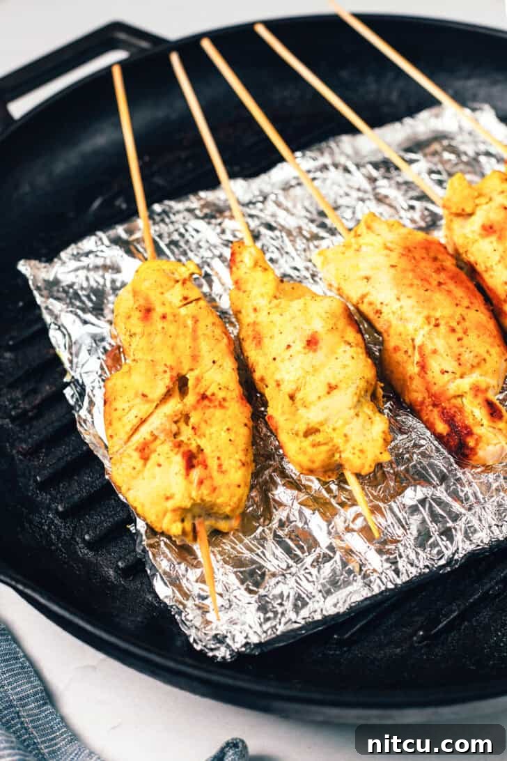 Four beautifully grilled chicken skewers resting on a baking sheet lined with foil, displaying their golden-brown char marks.