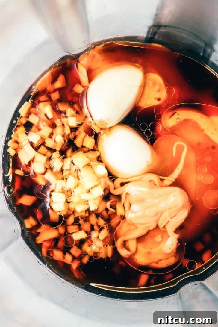 All the vibrant ingredients for the peanut sauce, including peanut butter, ginger, and soy sauce, placed inside a blender jar, poised for blending.