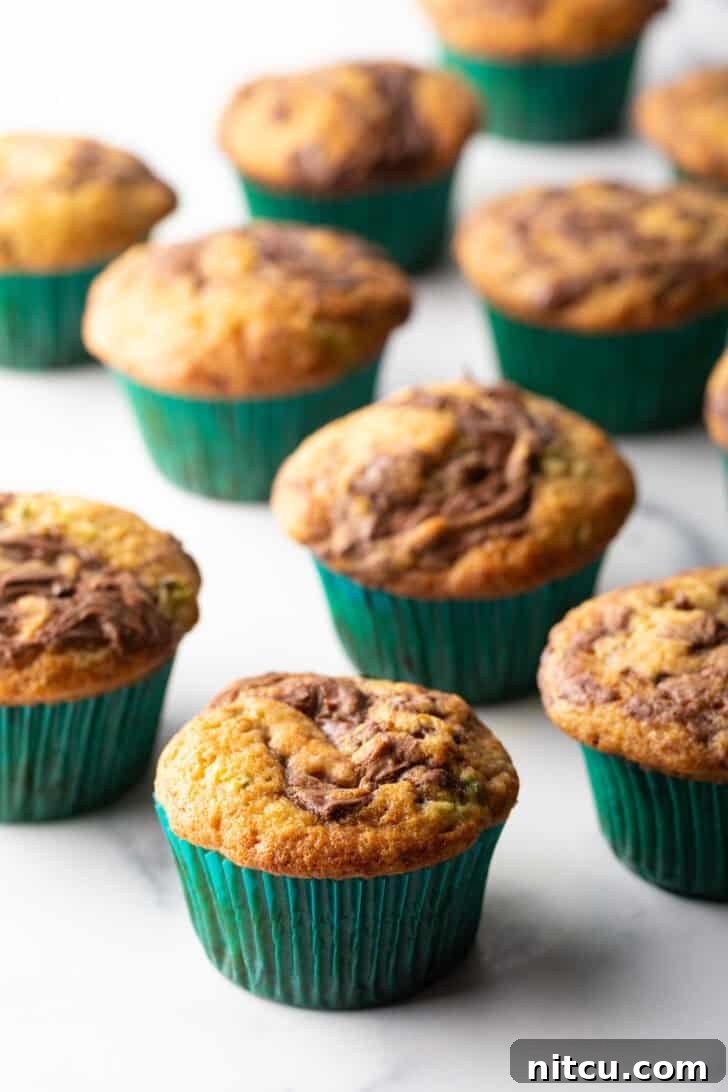 A dozen freshly baked chocolate zucchini muffins with elegant Nutella swirls, nestled in vibrant green cupcake wrappers, ready to be enjoyed.