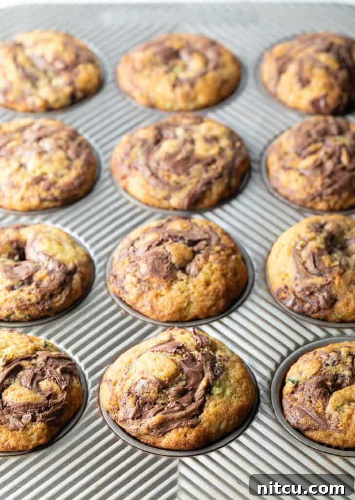 A dozen perfectly baked zucchini and Nutella swirl muffins, golden brown and enticing, still warm in their baking tin.