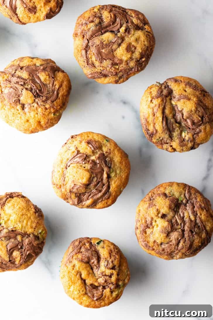 An overhead view of a dozen freshly baked chocolate zucchini muffins, beautifully swirled with chocolate, cooling in a baking tin.
