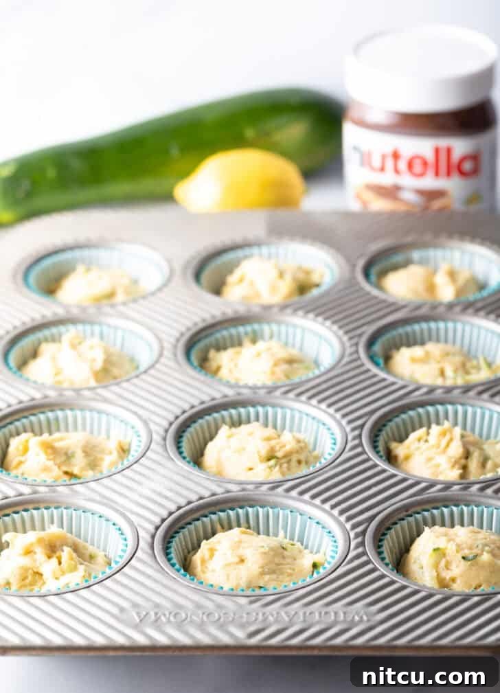 A muffin tin neatly lined with paper wrappers, each well filled with a portion of the moist zucchini muffin batter, awaiting the next step.