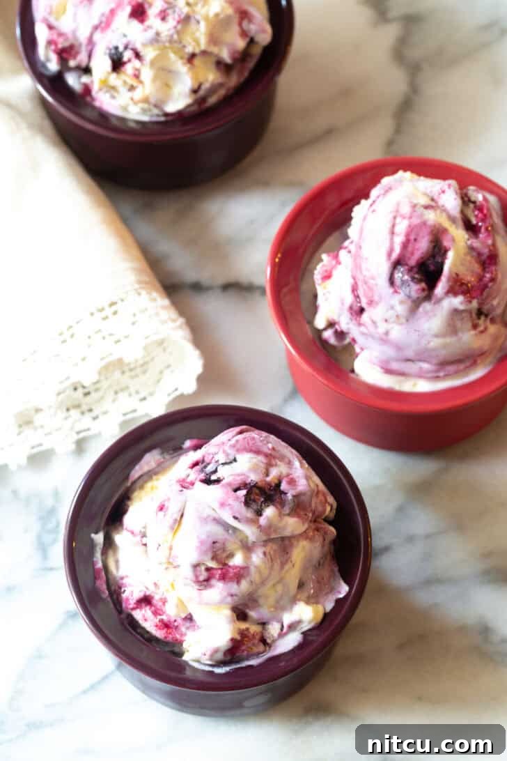 Top-down view of three bowls of creamy blueberry pie ice cream, each with a spoon, ready to be enjoyed.
