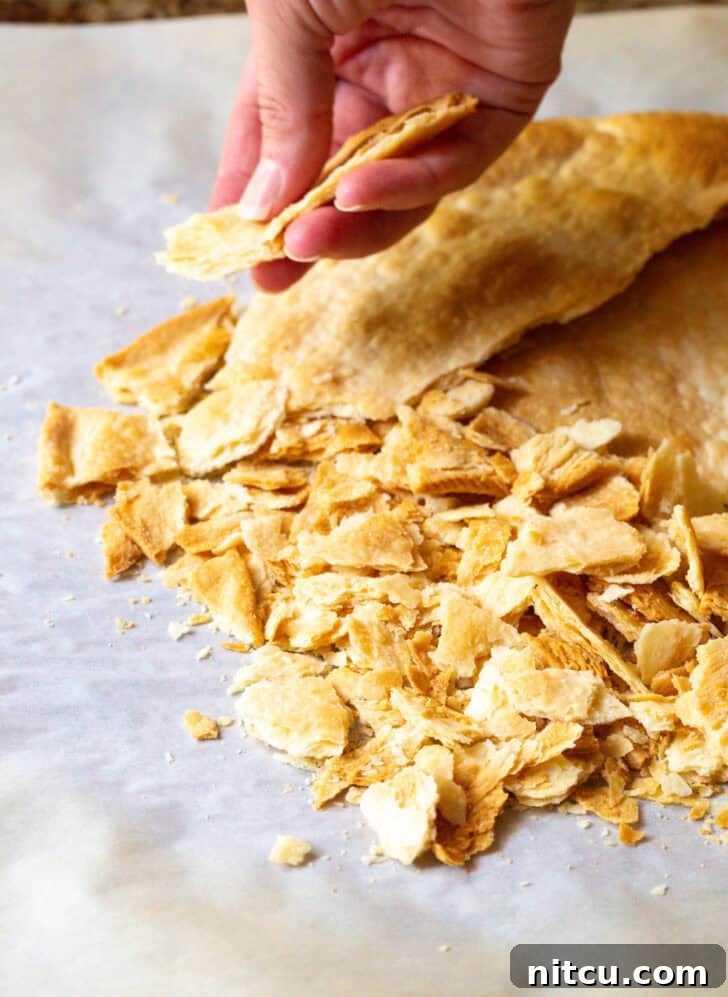 Hand cracking a piece of baked pie crust into small pieces over a bowl.