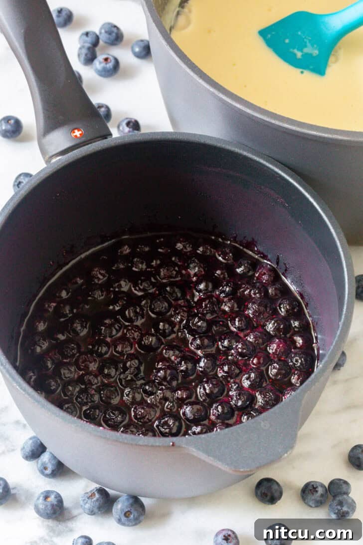 Cooking blueberries in a metal cooking pot on a stovetop.