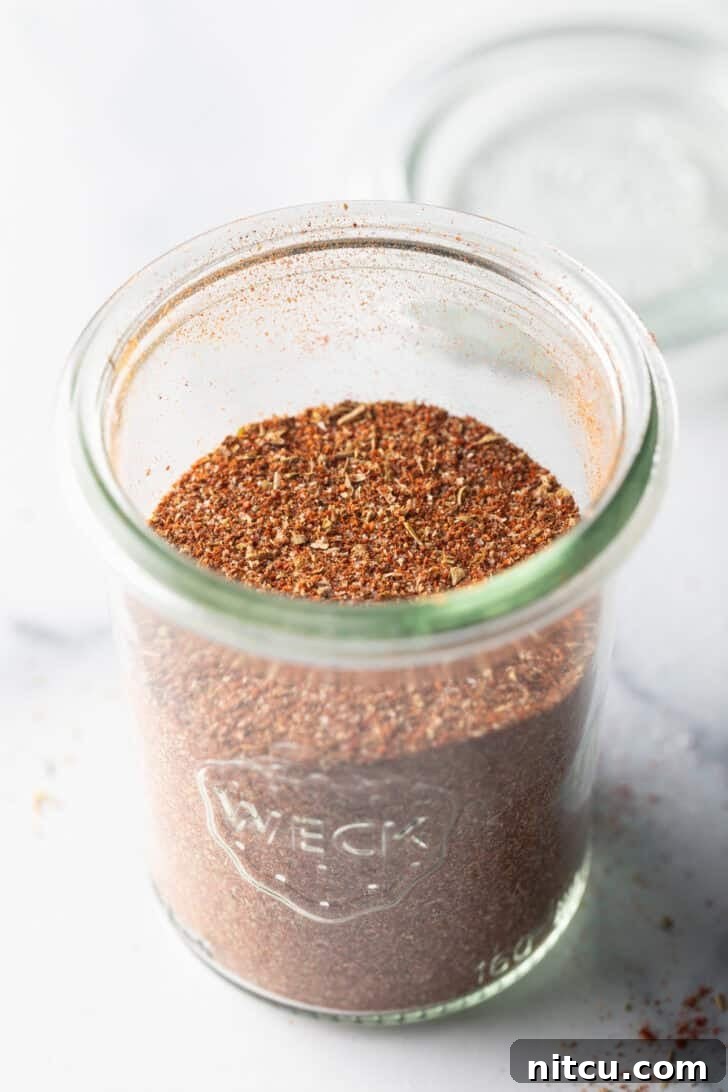 A tall glass jar brimming with freshly mixed homemade chicken taco seasoning, ready for storage.