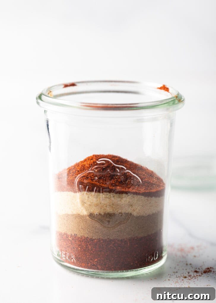 Individual layers of distinct spices visible in a clear glass jar, before mixing.