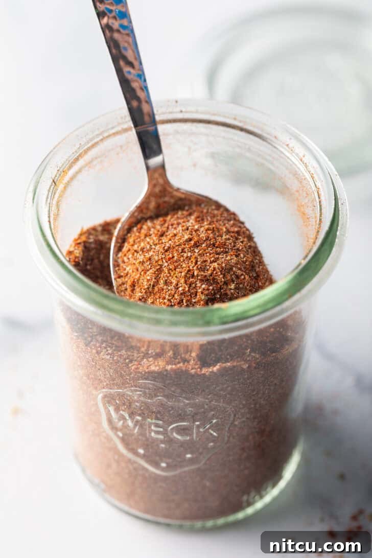 A spoon scooping a portion of the rich, aromatic chicken taco seasoning from a small glass jar.