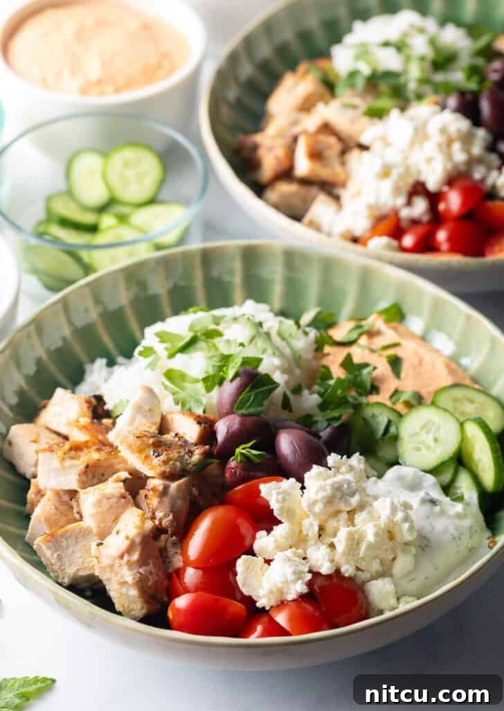 Greek chicken bowl with pieces of chicken, rice, sliced cherry tomatoes, kalamata olives, tzatziki sauce, cucumbers and feta cheese.