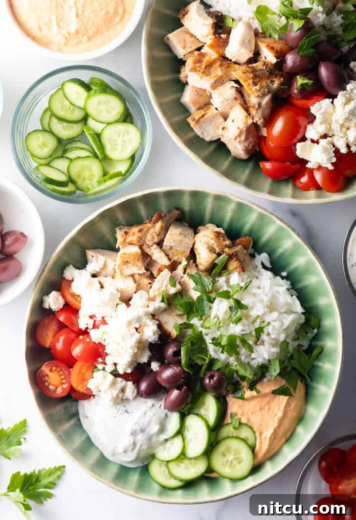 Greek chicken bowl with pieces of chicken, rice, sliced cherry tomatoes, kalamata olives, tzatziki sauce, cucumbers and feta cheese.