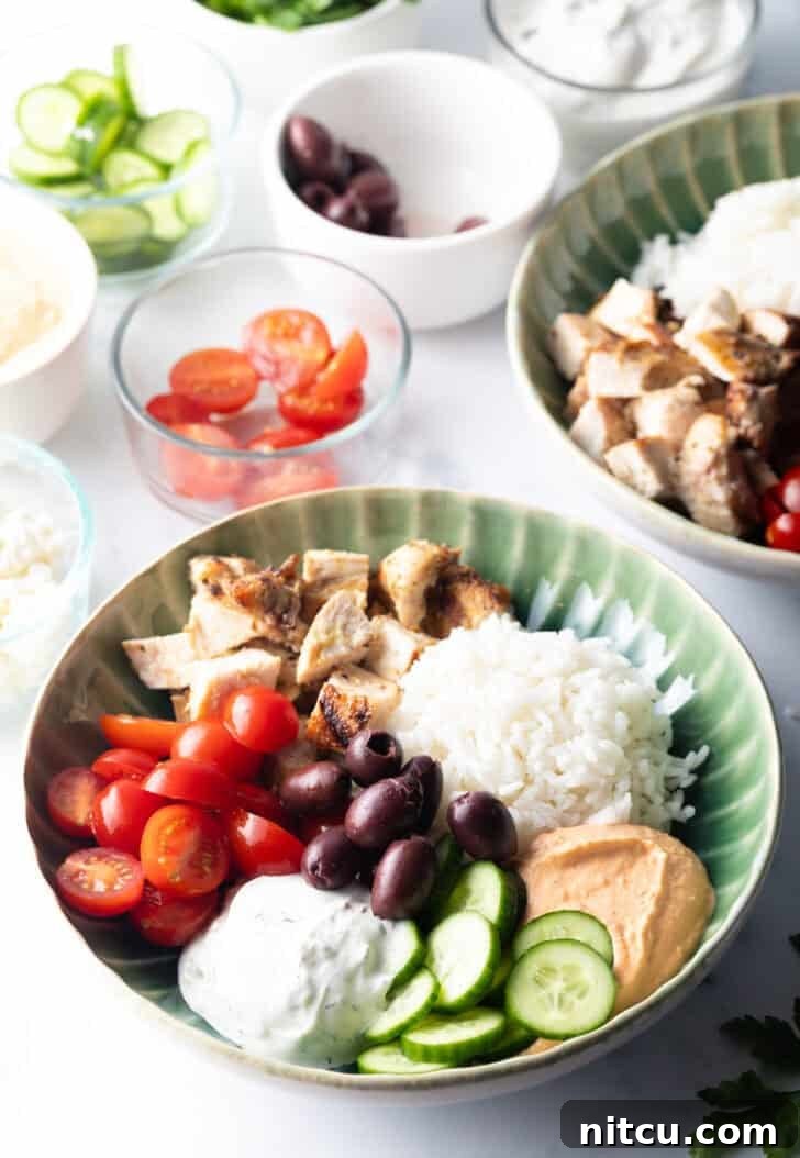 Greek chicken bowl with pieces of chicken, rice, sliced cherry tomatoes, kalamata olives, tzatziki sauce, cucumbers and feta cheese.
