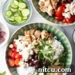 Greek chicken bowl with pieces of chicken, rice, sliced cherry tomatoes, kalamata olives, tzatziki sauce, cucumbers and feta cheese.