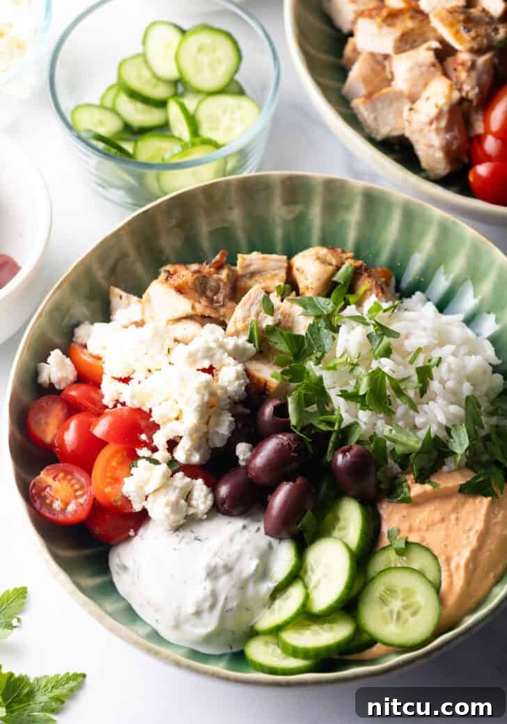 Top down view Mediterranean chicken bowl with pieces of chicken, rice, sliced cherry tomatoes, kalamata olives, tzatziki sauce, cucumbers and feta cheese.