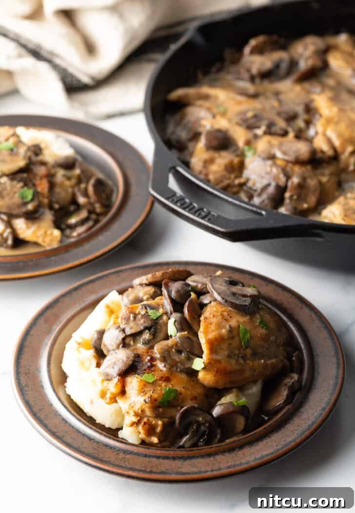 Brown plate with fluffy mashed potatoes, topped generously with two chicken breasts, tender sliced mushrooms, and rich gravy.