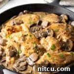 Mushroom Chicken - Cast iron skillet brimming with seared chicken breast pieces and sliced mushrooms in a rich brown gravy.