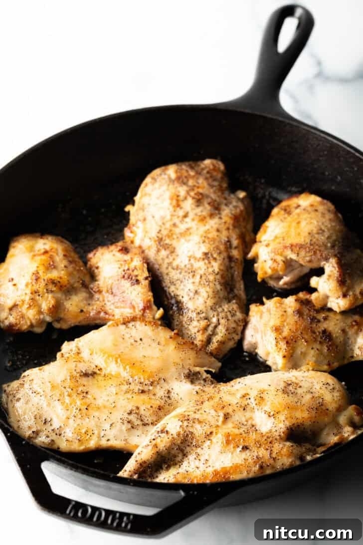 Four perfectly seared chicken breast cutlets resting in a cast iron skillet.