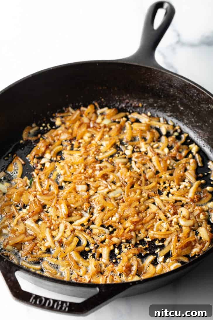 Diced onions and minced garlic browning in a cast iron skillet, releasing fragrant aromas.