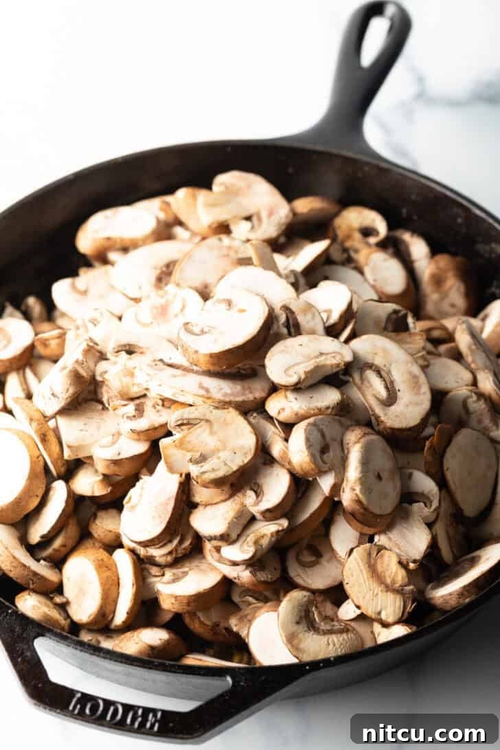 Freshly sliced button mushrooms being added to a cast iron skillet.