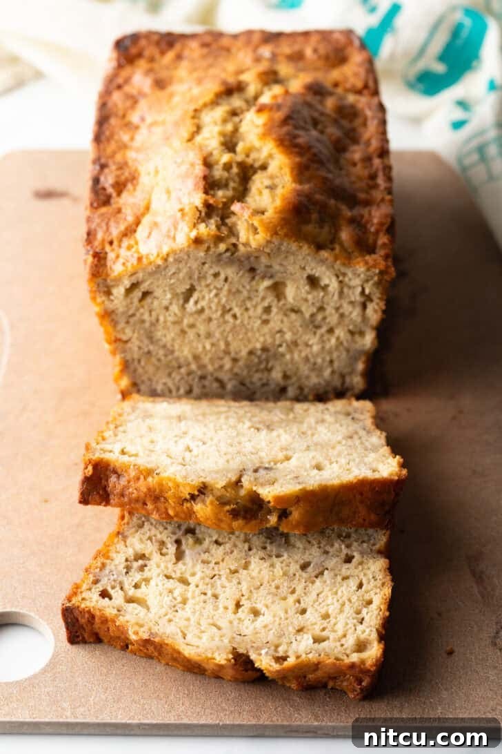 A freshly baked loaf of golden-brown banana bread on a wooden cutting board, with two inviting slices already cut and visible.