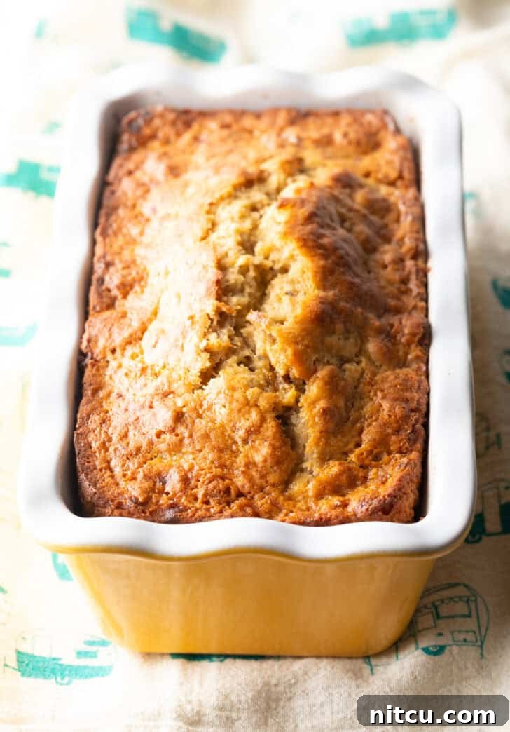 A beautifully baked 4-ingredient banana bread loaf, golden brown and still warm, resting in a white and yellow patterned loaf pan.
