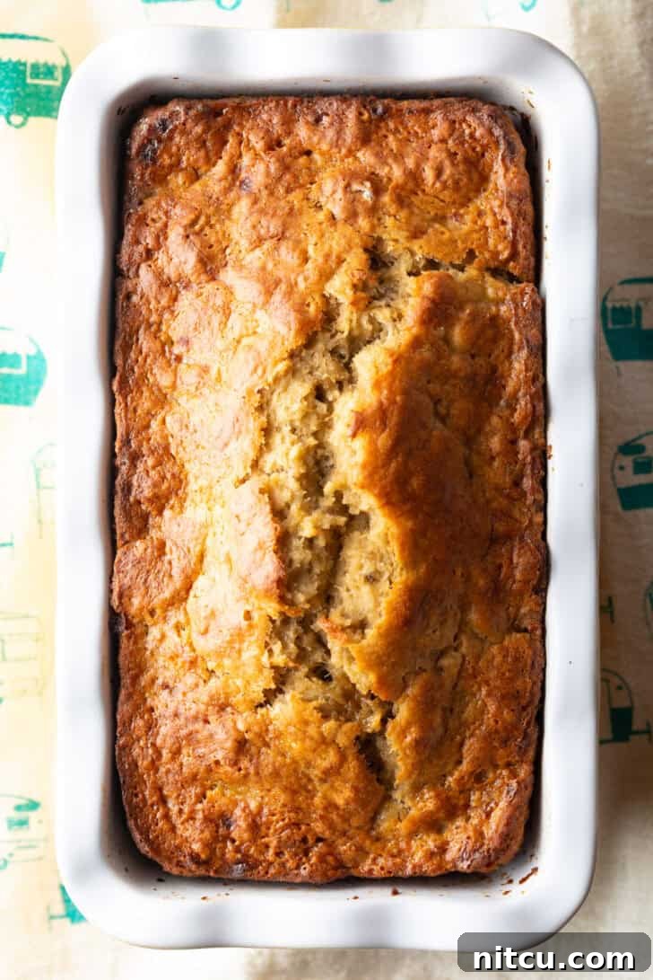 Top-down view of a perfectly baked 4-ingredient banana bread loaf, golden brown and enticing, still nestled in its white and yellow loaf pan.