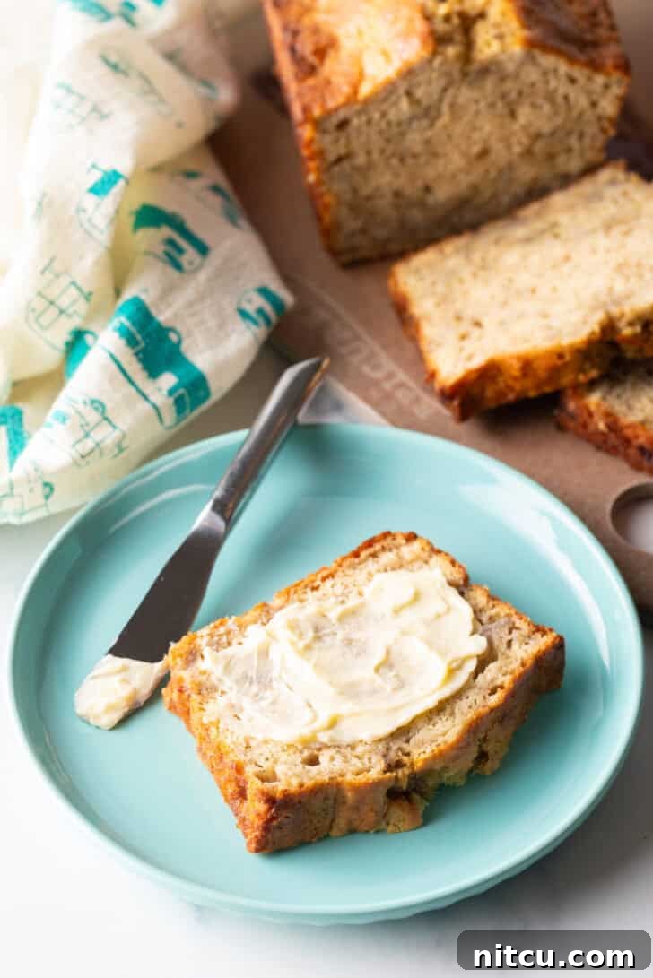 A beautifully sliced piece of 4-ingredient banana bread, glistening with melted butter, presented on a vibrant blue plate alongside a knife.